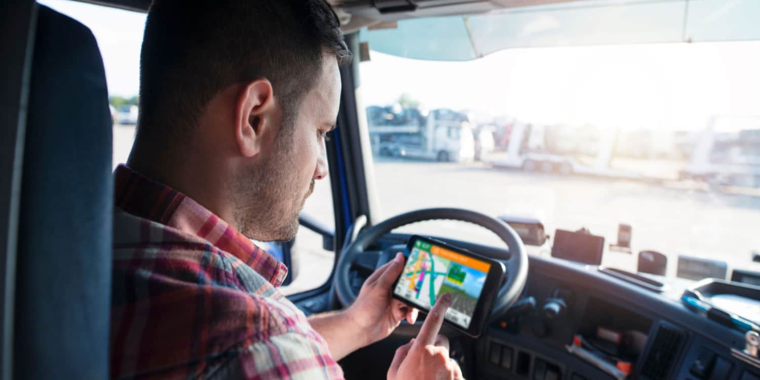 A trucker looking down at a GPS on his phone as he practices trip planning