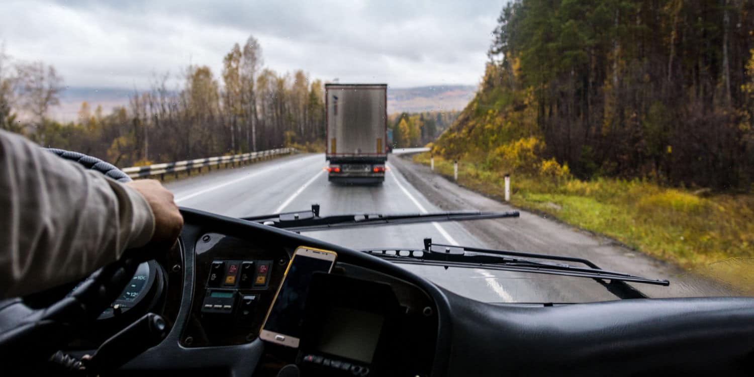 The dashboard of a semi-truck practicing defensive driving as they maintain a safe following distance behind another semi-truck