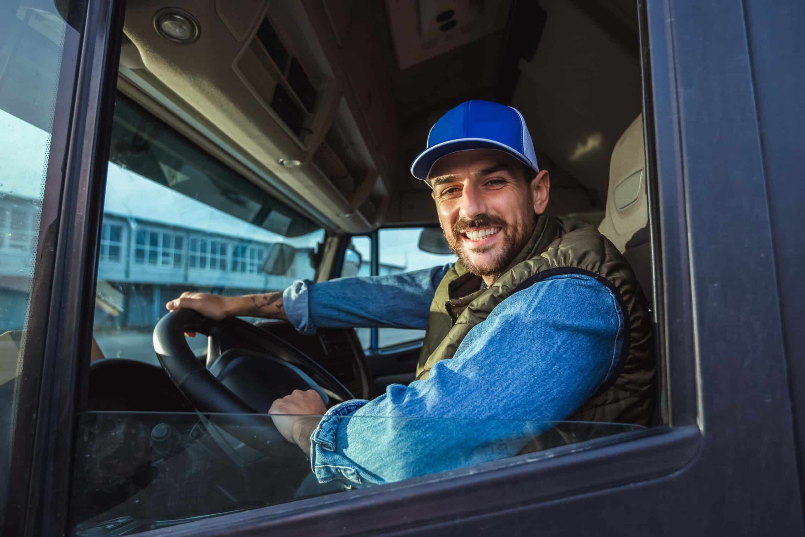 Truck driver in a blue cap and denim jacket, sitting behind the wheel of a large vehicle