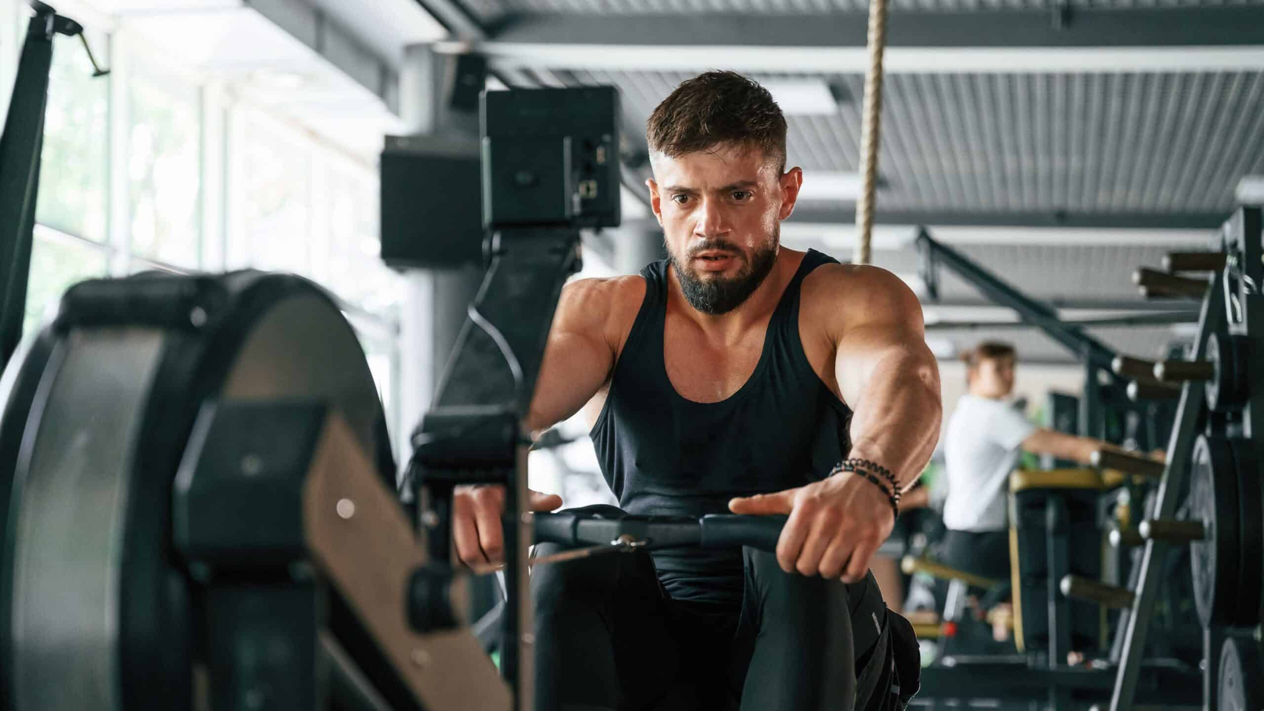 Focused man in a gym using a rowing machine for strength and cardio training.