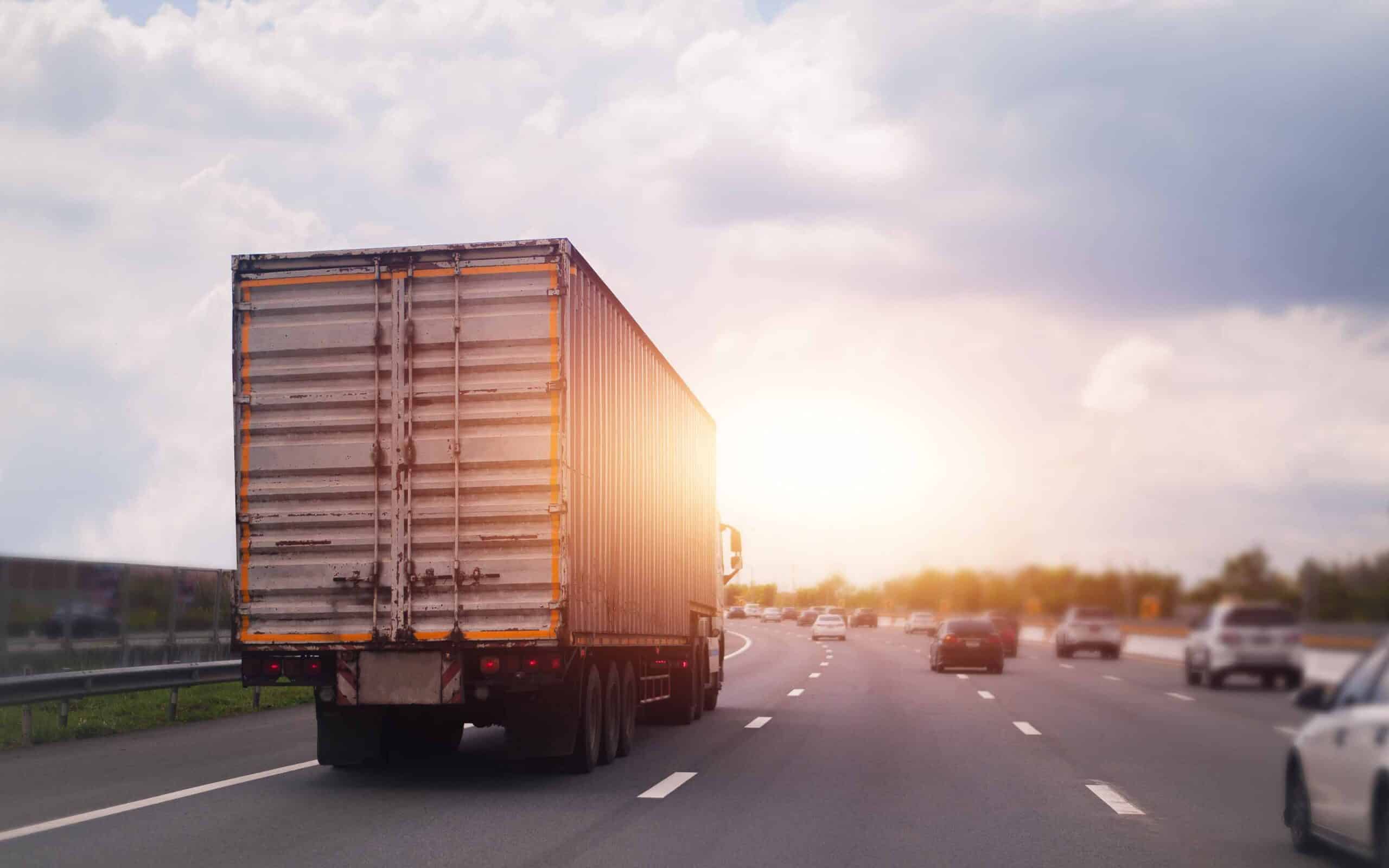 A semi-truck with a container trailer drives on a multi-lane highway into the sunset, symbolizing a smart CDL career move.